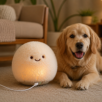 A golden retriever dog lies on a beige carpet next to a round, fluffy cream-colored pet lamp that glows with warm light. The lamp has a simple embroidered smiley face.